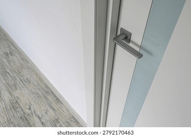 modern interior features a white concealed-mount door with a vertical frosted glass stripe; complemented by a matte grey lever handle and a light grey wood-patterned floor