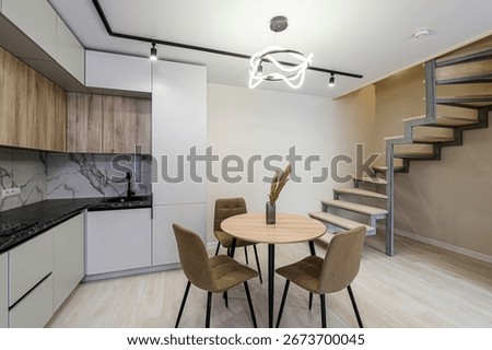 Modern interior featuring a kitchen area with cabinets and a black countertop, dining table with chairs, and a spiral staircase in a neutral color palette