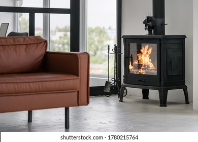 Modern interior house with bright living room, fire in new fireplace, comfortable leather couch on concrete floor against glass wall on background - Shutterstock ID 1780215764