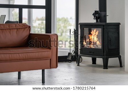 Modern interior house with bright living room, fire in new fireplace, comfortable leather couch on concrete floor against glass wall on background