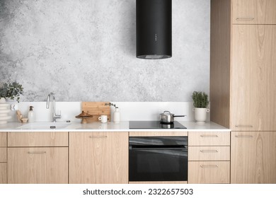 modern interior in kitchen room, wood cabinet with white countertop, glass ceramic hob, sink with water tap and hood extractor against grey wall