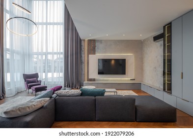 Modern Interior Of Living Room In Luxury Apartment. Cozy Sofa With Cushions. TV On Wall. Panoramic Window.