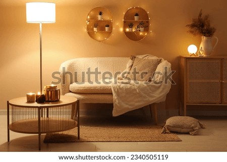 Modern interior of living room with stylish sofa and burning candles on table