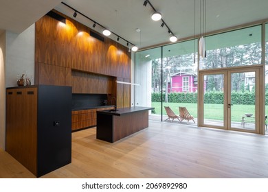 Modern interior of luxury private country house. Wooden and black kitchen. Garden view.