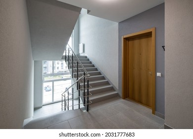 Modern interior of new entrance in residential building. Wooden door to apartment. Stairs and windows.