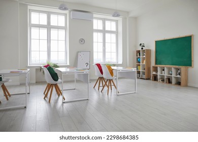 Modern interior of school class without people. Comfortable and ergonomic chairs and desks. Large green chalk board, shelves with accessories for educational process. Clock on the wall. - Shutterstock ID 2298684385