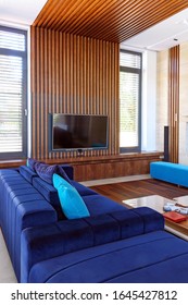 Modern Interior With Wood Slat  Ceiling, Comfortable Blue Furniture, Parquet, White Table And Wooden Tv Wall Unit. Living Room With Big Windows And Wooden Details