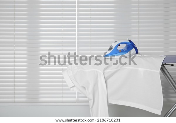 Modern iron and clean shirt on board near window,\
space for text