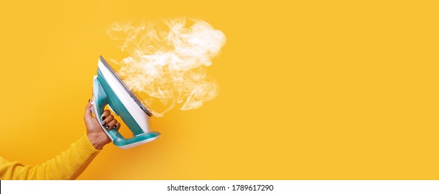 modern iron with steam in hand over yellow background, panoramic mock-up image