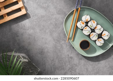 Modern japanese food concept. Maki sushi on ceramic plate with soy sauce and chopsticks on stone background. Aesthetic composition with sushi roll on dark concrete backdrop. Yin yang maki roll