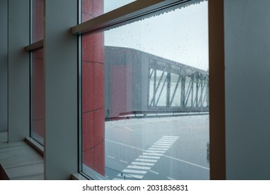 Modern jetway located on airfield behind wet window of aerodrome on rainy day