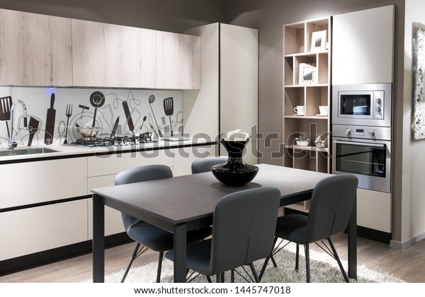Modern kitchen with artistic splash\
back above a white counter, built in cabinets and appliances and a\
central table and chairs in a stylish beige brown\
decor