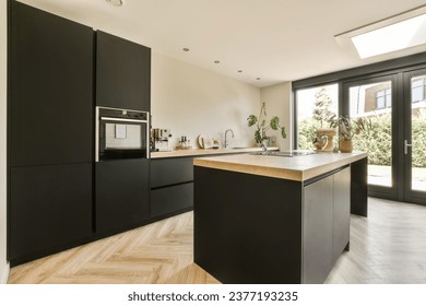 a modern kitchen with black cabinetry and wood flooring in an open plan living room, dining area on the other side - Powered by Shutterstock