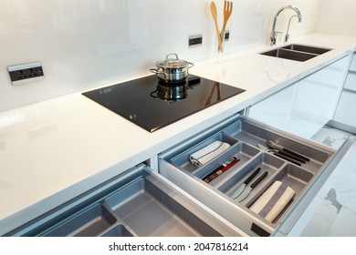 Modern kitchen with black induction stove, cooker, built in cooktop, Induction hob install on white countertop. opened drawer with accessories inside, solution for kitchen storage, White kitchen.