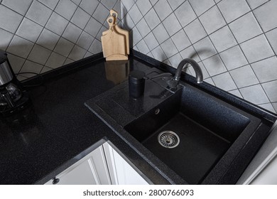 modern kitchen corner features black stone sink with curved faucet, wooden cutting board, matte black cup, and grey tiled backsplash. coffee maker sits to the left