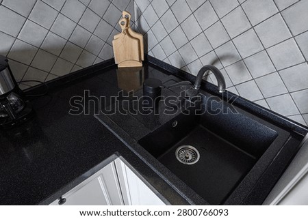 modern kitchen corner features black stone sink with curved faucet, wooden cutting board, matte black cup, and grey tiled backsplash. coffee maker sits to the left