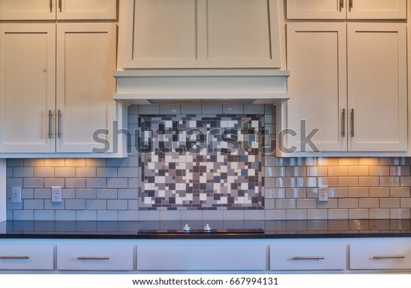 Modern kitchen counter\
and cabinets with granite counters, white cabinets, cook top,\
subway tile back splash.