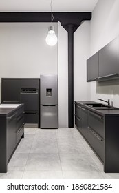 Modern Kitchen With Dark Gray Cupboards, Drawers And Countertops, Silver Fridge And Gray Floor Tiles In Tall Loft Apartment With Black Pillar