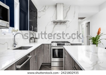A modern kitchen detail with glossy blue and wood cabinets, stainless steel appliances, and a marble countertop and backsplash. No brands or logos.