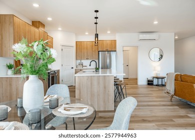 Modern kitchen and dining room interior staged for real estate with kitchen island bar stools stainless appliances hardwood floor sink pendant lighting bright sunny mixed wood cabinets table setting