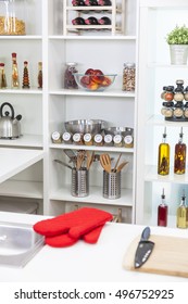 A Modern Kitchen Empty No People, With Red Oven Gloves, Oils, Olive Oil, Wine, Fruit, Spices, Equipment, Utensils, Kettle, Knife And Chopping Board