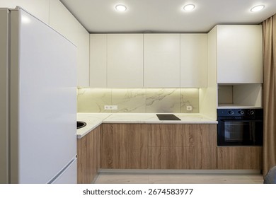 modern kitchen featuring white upper cabinets, wood-grain lower cabinets, and a marble-patterned backsplash. A built-in oven and white refrigerator are also visible