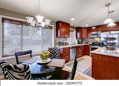 Modern Kitchen Interior With Bright Wooden Cabinets And Steel Appliances. Mosaic Back Splash Trim Blend Perfectly With Granite Tops. Black Round Dining Table With Black And Zebra Chairs