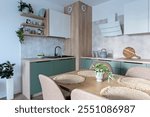 Modern kitchen interior with dining table and chairs. Green and white furniture with cabinet, kitchen sink and beige tiles on the wall.  Design in new apartment. Real estate.