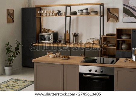 Modern kitchen interior featuring induction cooktop, oven, countertop with frying pan, baked goods, shelves with dishes, glassware, small appliances, potted plant, decorative wall art