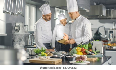 In the Modern Kitchen Team of Cooks Use Tablet Computer For Recipes, They Smile and Have Discussion. Kitchen is Full of Food Ingredients, Vegetables, Meat, Boiling Soup. - Powered by Shutterstock