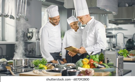 In the Modern Kitchen Team of Cooks Use Tablet Computer For Recipes, They Smile and Have Discussion. Kitchen is Full of Food Ingredients, Vegetables, Meat, Boiling Soup. - Powered by Shutterstock