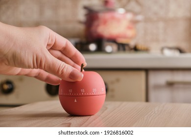 modern kitchen timer apple shaped on the background of the kitchen, stove and pans, Closeup of female hands. Housewife or chef using timer eggtimer, round alarm clock