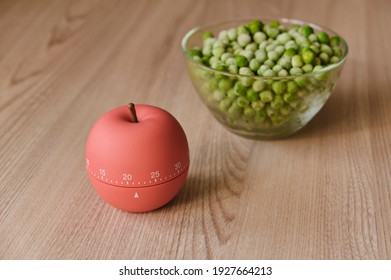 modern kitchen timer apple shaped on the background of the kitchen and green peas are thawed in a dish for cooking, using timer eggtimer, round alarm clock