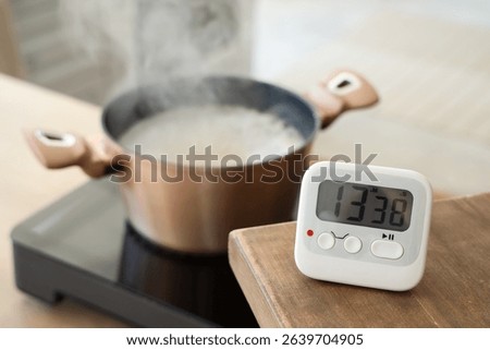 Modern kitchen timer on table against cooking pot in room, closeup