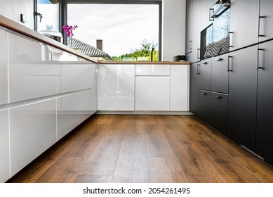 A modern kitchen with white and black fronts and a large corner window, vinyl panels on the floor. - Shutterstock ID 2054261495