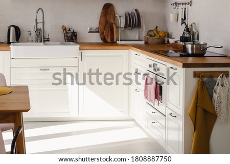 Modern kitchen with white cabinets, wood counter and dining table in sunlight in daytime. Full set of kitchen equipment.