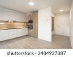 A modern kitchen with white cabinets, wooden countertops, built-in appliances, under-cabinet lighting, light wooden flooring, an entryway with a white door, and a wooden bench.