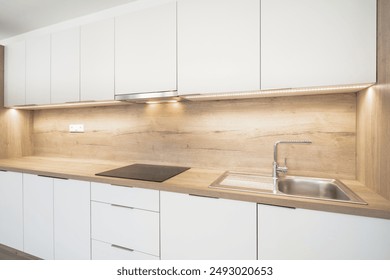 Modern kitchen with white cabinets, a wooden countertop, under-cabinet lighting, a ceramic hob, and a stainless steel sink. Clean, contemporary design with minimalist aesthetics and functional layout. - Powered by Shutterstock