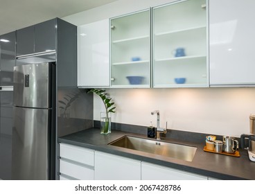 Modern Kitchen With White Furniture And Glass Door Wall Cabinet And Have Under Mount Kitchen Sink   Worktop, Stainless Steel Sink 1 Bowl And Tap Water On In The Kitchen. Black Granite Countertop.