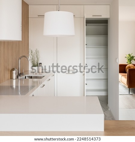 Modern kitchen with white furniture and lamp, mirror wall and open doors to pantry