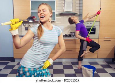 Modern kitchen - woman pretend to sing song with ladle and smiling young man cleaning the floor at home and play like guitar with  mop - Powered by Shutterstock