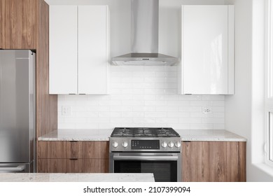 A Modern Kitchen With Wood And White Cabinets, A Subway Tile Backsplash, And Stainless Steel Appliances.