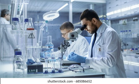 In a Modern Laboratory Two Scientists Conduct Experiments. Chief Research Scientist Adjusts Specimen in a Petri Dish and Looks on it Into Microscope.