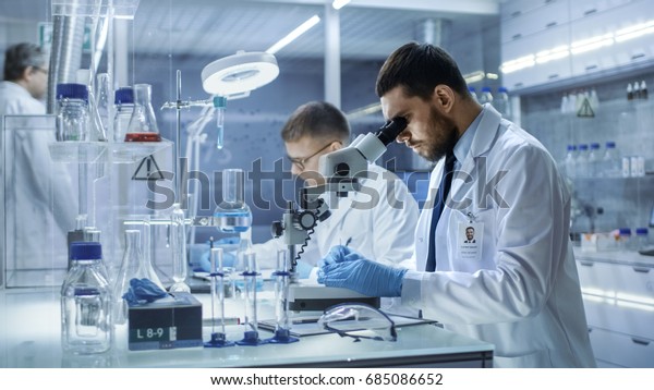 In a Modern Laboratory Two Scientists\
Conduct Experiments. Chief Research Scientist Adjusts Specimen in a\
Petri Dish and Looks on it Into\
Microscope.