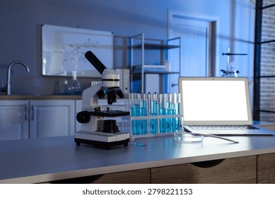 Modern laboratory workspace with microscope, test tubes, and laptop for scientific research and analysis in a darkened room