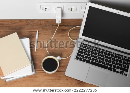 Modern laptop charging on wooden table, above view