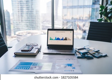 Modern laptop computer with infographic statistics for business displayed on screen staying on table desktop in office interior of corporate company, netbook and wat of money as concept of wealthy - Shutterstock ID 1827105584