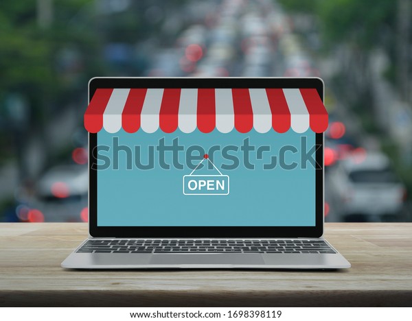 Modern laptop\
computer with online shopping store graphic and open sign on wooden\
table over blur of rush hour with cars and road in city, Business\
internet shop online\
concept