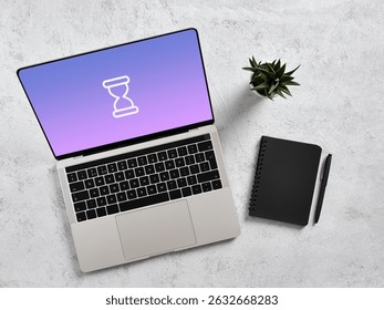 Modern laptop displaying hourglass icon, symbolizing waiting or processing, placed on a desk alongside a notebook and pen, suggesting work or productivity