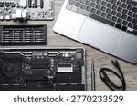 Modern laptop, internal electrical components, screwdriver and set of bits on wooden table, flat lay